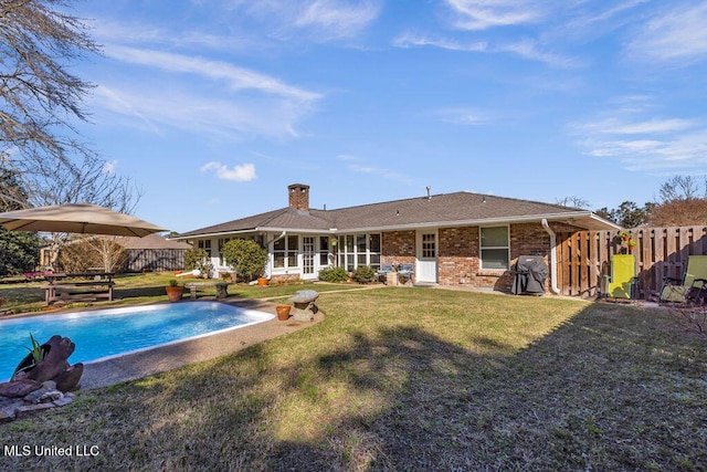 rear view of house with fence, a lawn, a fenced in pool, and brick siding