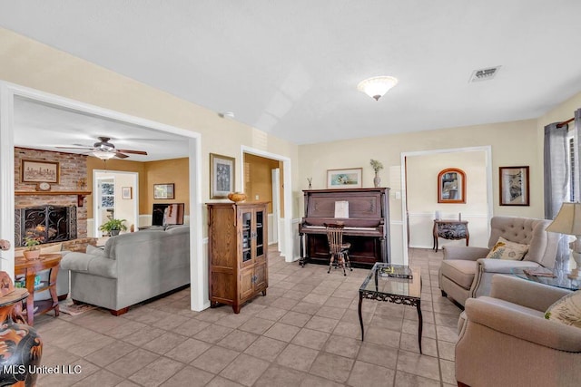 living area featuring a brick fireplace, visible vents, ceiling fan, and light tile patterned floors