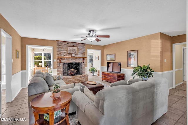 tiled living room featuring a ceiling fan, a wainscoted wall, and a fireplace