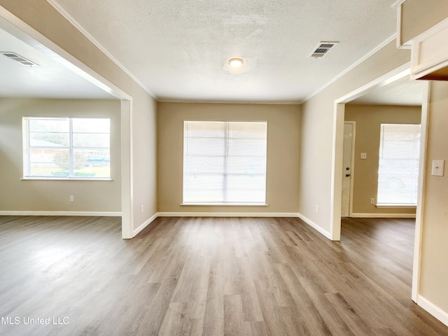 empty room featuring visible vents, wood finished floors, and ornamental molding