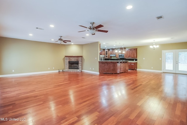 unfurnished living room with ceiling fan with notable chandelier, a fireplace, light hardwood / wood-style floors, and french doors