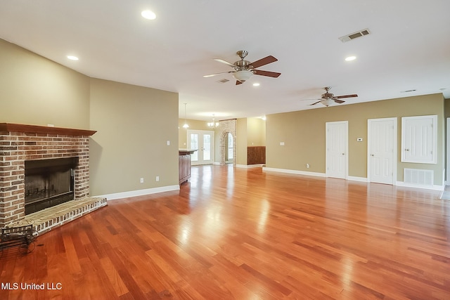 unfurnished living room with a brick fireplace, ceiling fan with notable chandelier, and light hardwood / wood-style flooring