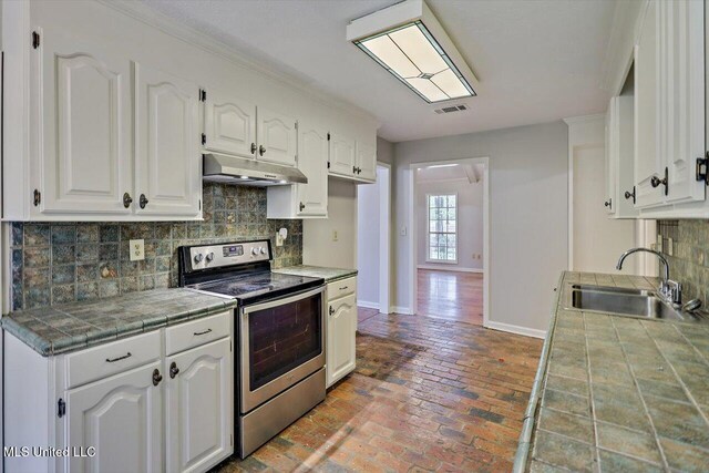 kitchen with stainless steel range with electric cooktop, a sink, tile countertops, baseboards, and under cabinet range hood