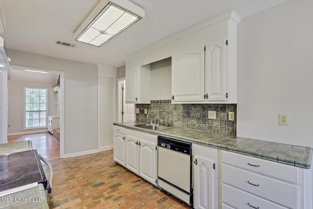 kitchen with backsplash, white dishwasher, a sink, brick floor, and white cabinetry