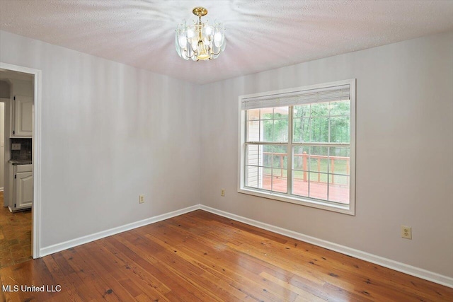 unfurnished room featuring baseboards, wood-type flooring, a textured ceiling, and a notable chandelier