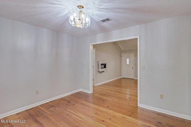 empty room with visible vents, heating unit, baseboards, light wood-style flooring, and a notable chandelier