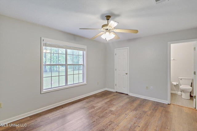 unfurnished bedroom with a ceiling fan, baseboards, wood finished floors, and ensuite bath