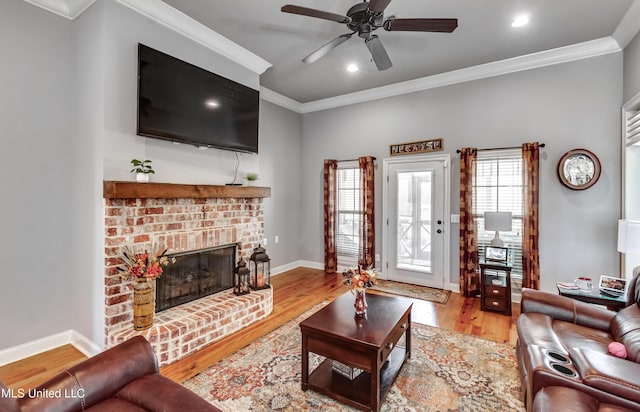 living area with a ceiling fan, wood finished floors, a fireplace, crown molding, and baseboards