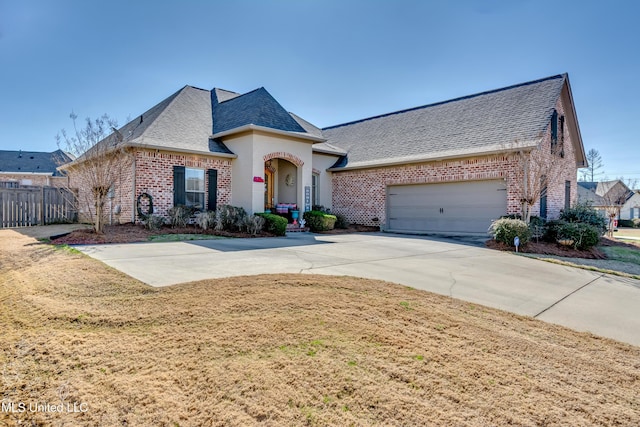 french country home featuring a front yard, fence, driveway, a garage, and brick siding