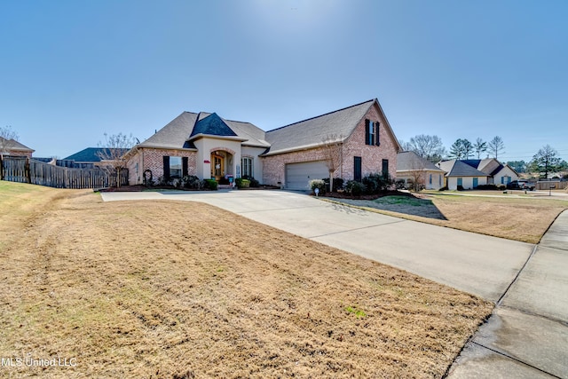 french provincial home featuring a front yard, fence, driveway, an attached garage, and brick siding