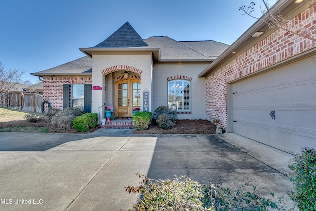 french country home with fence, roof with shingles, concrete driveway, french doors, and brick siding