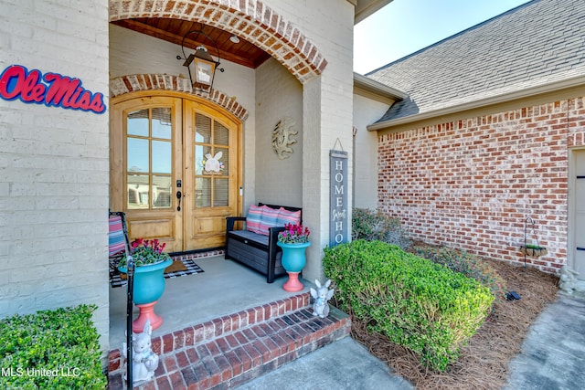 view of exterior entry featuring french doors, brick siding, and roof with shingles