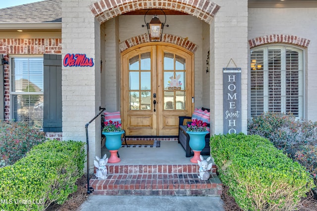 entrance to property featuring french doors, brick siding, and a shingled roof