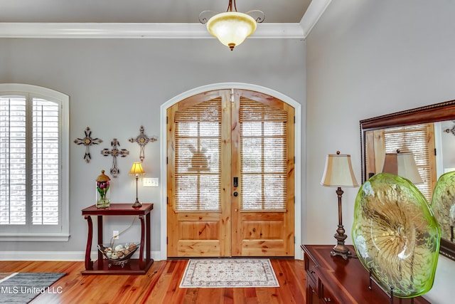 entrance foyer with crown molding, wood finished floors, arched walkways, and baseboards