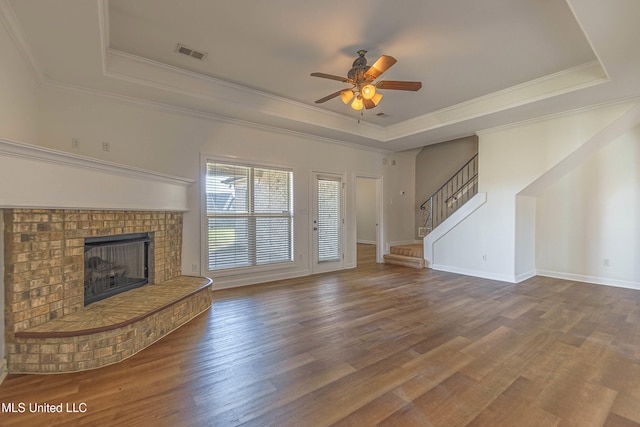 unfurnished living room featuring wood finished floors, stairs, ceiling fan, visible vents, and a raised ceiling