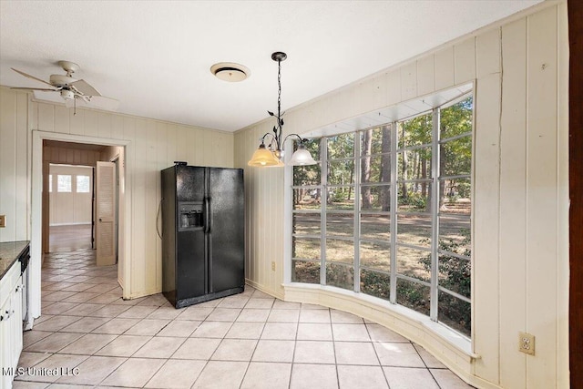 kitchen with wooden walls, decorative light fixtures, black fridge with ice dispenser, and plenty of natural light