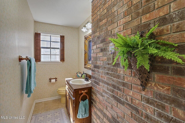 bathroom with toilet, vanity, brick wall, baseboards, and tile patterned floors