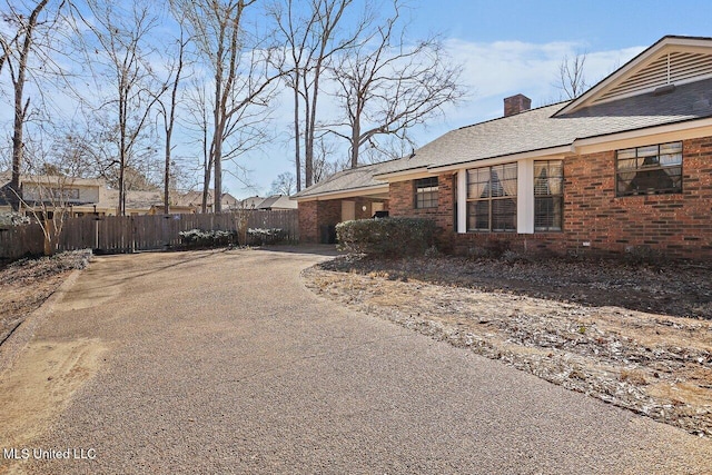 view of side of home with driveway, a chimney, fence, and brick siding