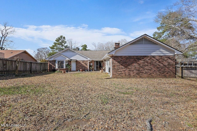 rear view of house featuring brick siding, fence, a chimney, and a lawn