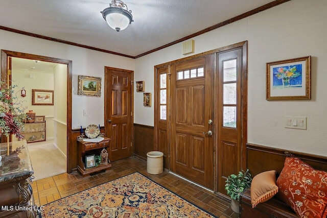 entryway with a wainscoted wall, wood walls, a textured ceiling, and crown molding