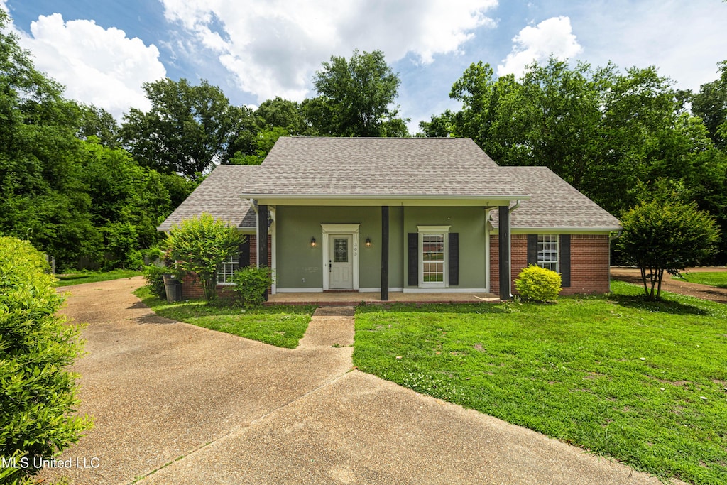 view of front of house featuring a front yard, a shingled roof, brick siding, covered porch, and concrete driveway