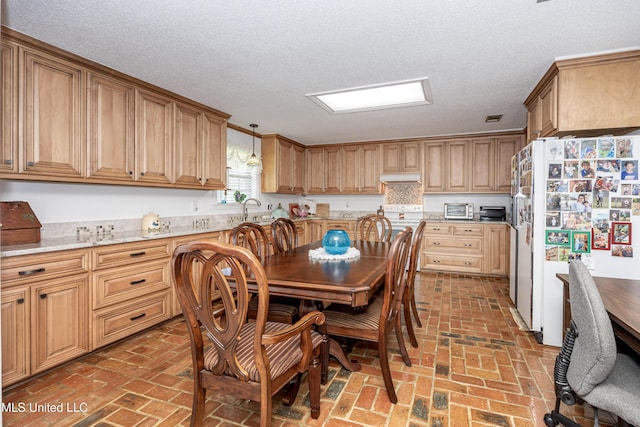 10001 Echo Glen Dr, Moss Point, MS 39562 - kitchen with freestanding refrigerator, under cabinet range hood, brick flooring, a textured ceiling, and light stone countertops