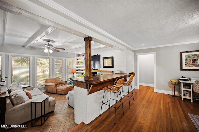 interior space featuring a kitchen bar, decorative columns, a textured ceiling, ceiling fan, and hardwood / wood-style flooring