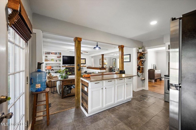 kitchen with kitchen peninsula, appliances with stainless steel finishes, white cabinetry, dark stone counters, and ornate columns