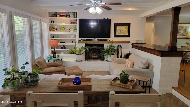 living area with beam ceiling, a brick fireplace, a ceiling fan, and built in features