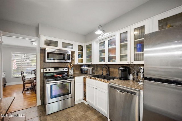 kitchen featuring a sink, stainless steel appliances, tasteful backsplash, glass insert cabinets, and white cabinets