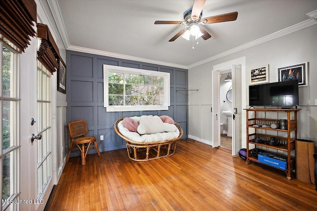 sitting room with ornamental molding, a decorative wall, a ceiling fan, and light wood-style floors