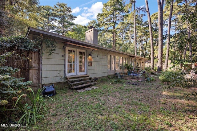 back of property with fence, entry steps, french doors, and a chimney