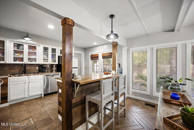 kitchen featuring tasteful backsplash, decorative columns, hanging light fixtures, white cabinetry, and stainless steel dishwasher