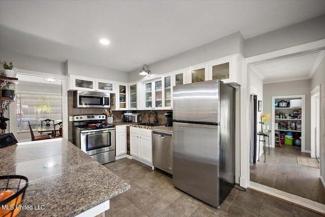kitchen featuring a sink, stainless steel appliances, tasteful backsplash, white cabinetry, and glass insert cabinets