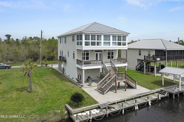 back of house featuring central air condition unit, a deck with water view, a patio area, a sunroom, and a lawn