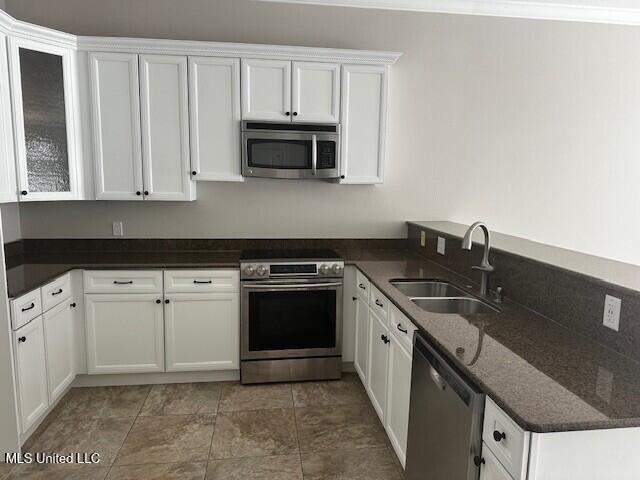 kitchen with a sink, glass insert cabinets, dark stone counters, stainless steel appliances, and white cabinetry