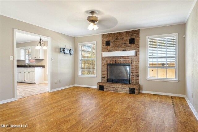 310 Lafayette St, Senatobia, MS 38668 - unfurnished living room with light wood-style floors, a brick fireplace, a healthy amount of sunlight, and ornamental molding