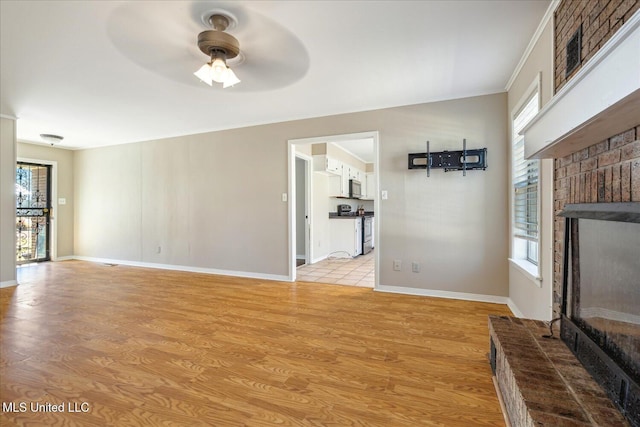 310 Lafayette St, Senatobia, MS 38668 - unfurnished living room featuring a brick fireplace, a healthy amount of sunlight, ceiling fan, and light wood-style flooring