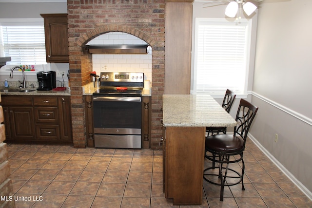 kitchen with a sink, a ceiling fan, stainless steel range with electric stovetop, a breakfast bar, and dark tile patterned floors