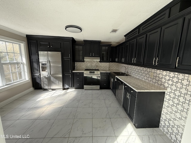 kitchen featuring visible vents, marble finish floor, under cabinet range hood, dark cabinetry, and appliances with stainless steel finishes