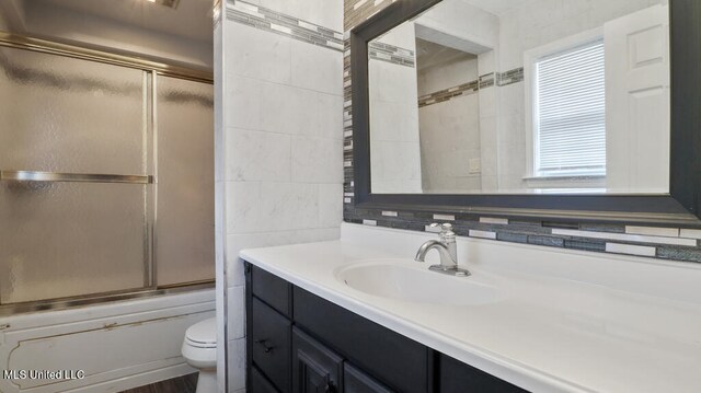 full bathroom with enclosed tub / shower combo, vanity, toilet, and tile walls