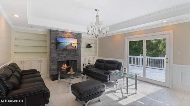 living room with a stone fireplace, ornamental molding, a notable chandelier, a raised ceiling, and built in shelves