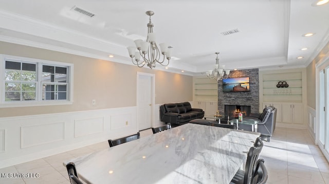 dining space with a stone fireplace, a chandelier, light tile patterned floors, a raised ceiling, and built in shelves