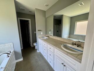 full bathroom with double vanity, a bath, baseboards, and concrete floors