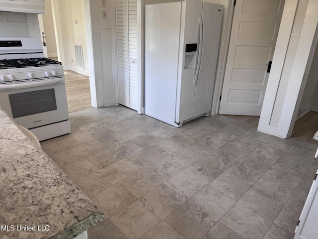 kitchen featuring white appliances, ventilation hood, and light stone countertops