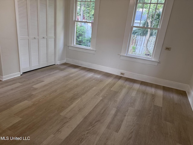 unfurnished bedroom featuring light wood finished floors, baseboards, and a closet