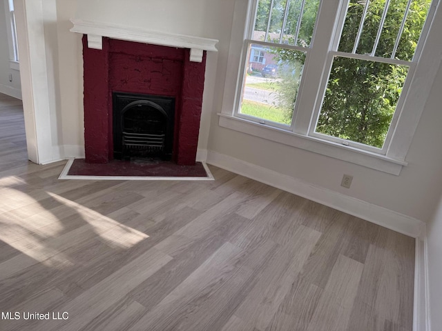 unfurnished living room featuring wood finished floors, baseboards, and a fireplace with flush hearth