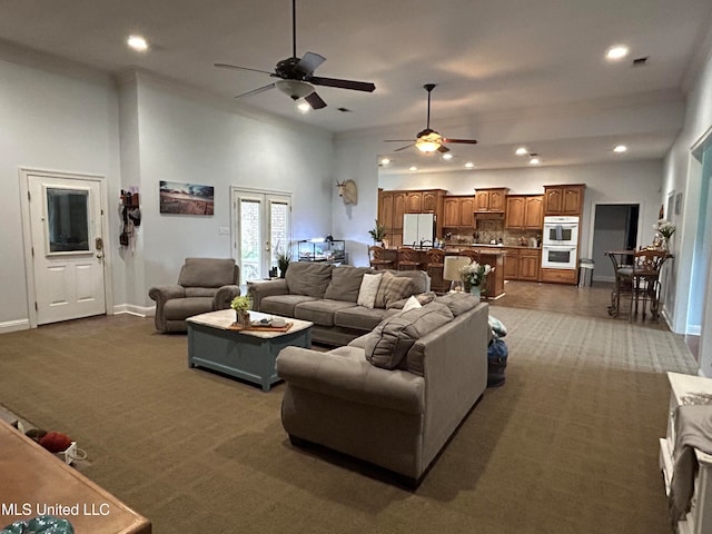 living room featuring a towering ceiling, ceiling fan, and dark colored carpet