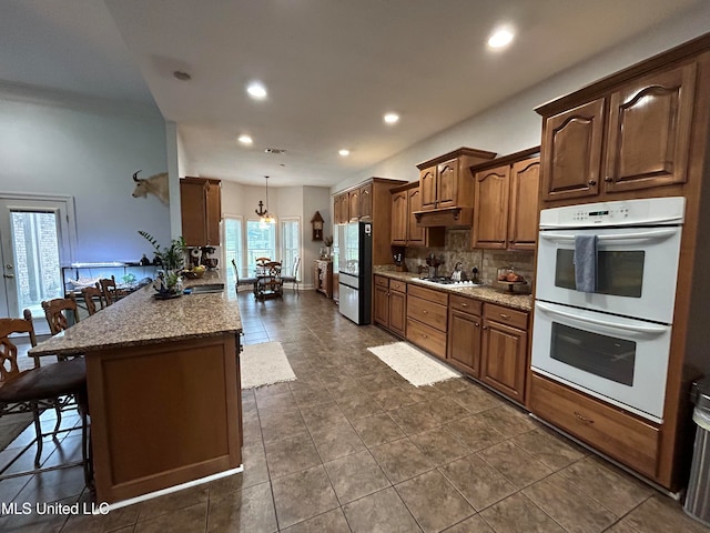 kitchen featuring light stone countertops, pendant lighting, decorative backsplash, a kitchen breakfast bar, and white appliances