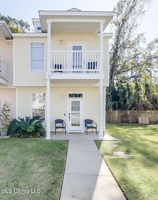 rear view of house with a balcony, a patio area, and a lawn